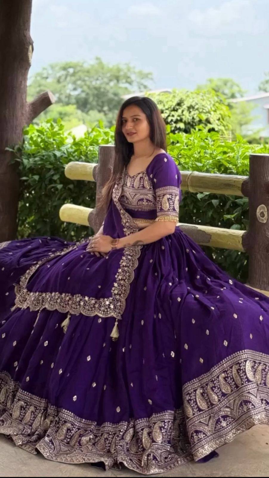 Woman in a purple traditional outfit with silver details sitting outdoors.