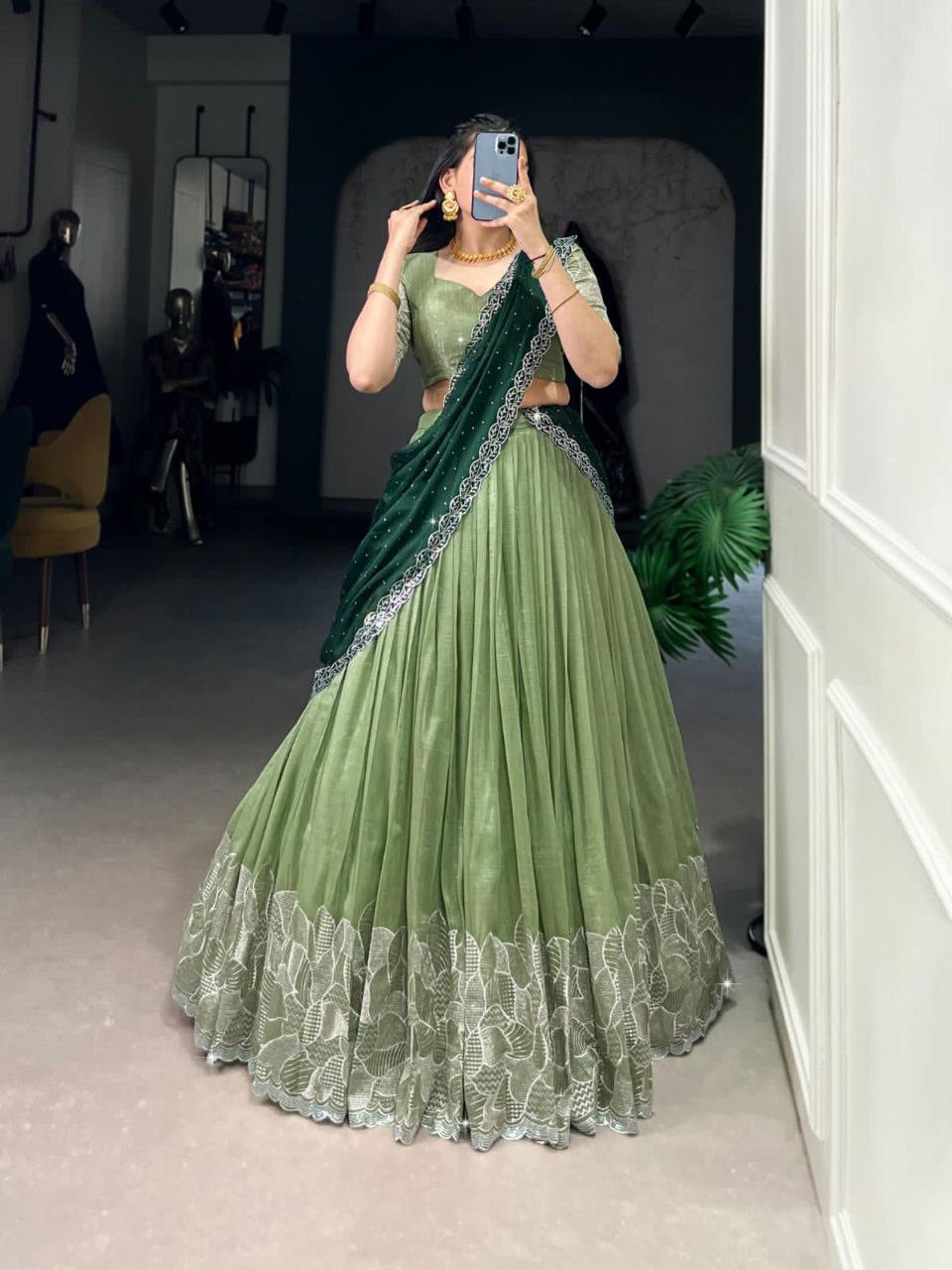 Woman wearing an elegant olive green designer lehenga saree with intricate white embroidery and dark green drape.